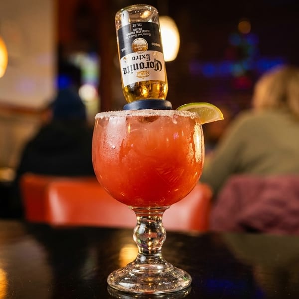 Red cocktail with an inverted Corona bottle and lime wedge on a table in a restaurant.