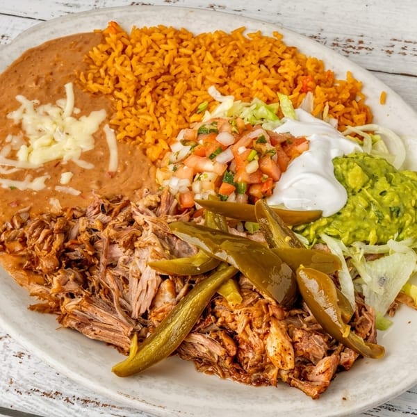 Plate of shredded pork, rice, refried beans, guacamole, sour cream, pico de gallo, and pickled green peppers.