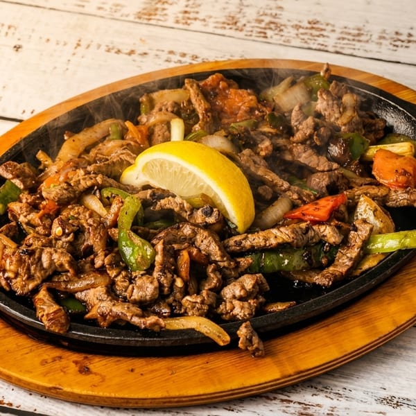 Sizzling beef fajitas with peppers, onions, and a lemon wedge on a wooden board.