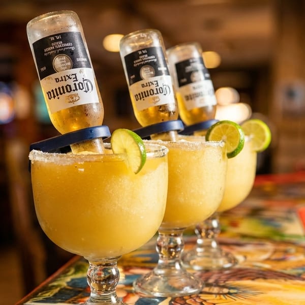 Three frosty margaritas with upside-down Corona beers and lime wedges on a patterned table.