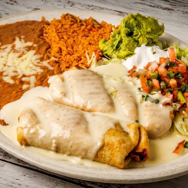 Two chimichangas covered in white sauce, served with refried beans, rice, guacamole, and pico de gallo.
