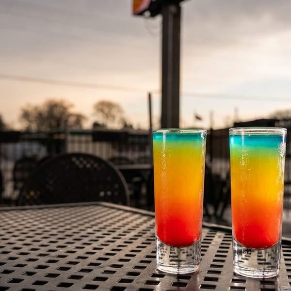Two vibrant, layered rainbow cocktails on an outdoor patio table at dusk.
