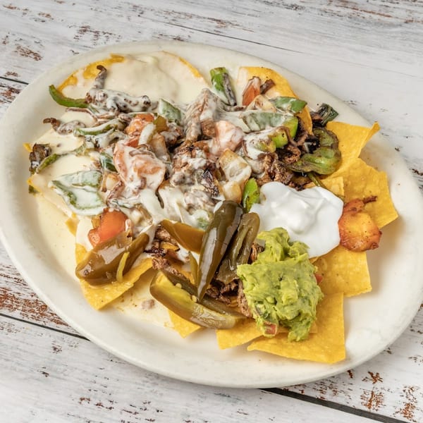 Nachos topped with melted cheese, meat, peppers, jalapeños, guacamole, and sour cream on a white plate.