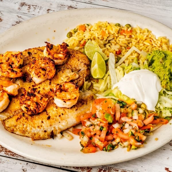 Plate of grilled fish and shrimp with rice, guacamole, sour cream, pico de gallo, and lime.